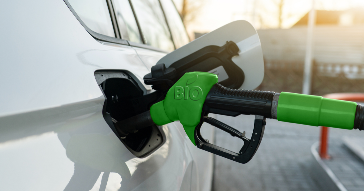 Green biofuel pump nozzle inserted into a white vehicle’s fuel tank, representing clean energy and sustainable transportation.