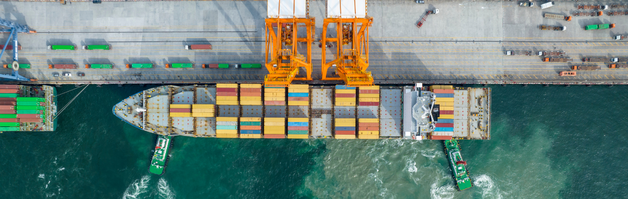  Luftaufnahme eines an einem Hafen angedockten Frachtschiffs mit bunten Containern und Kränen. 