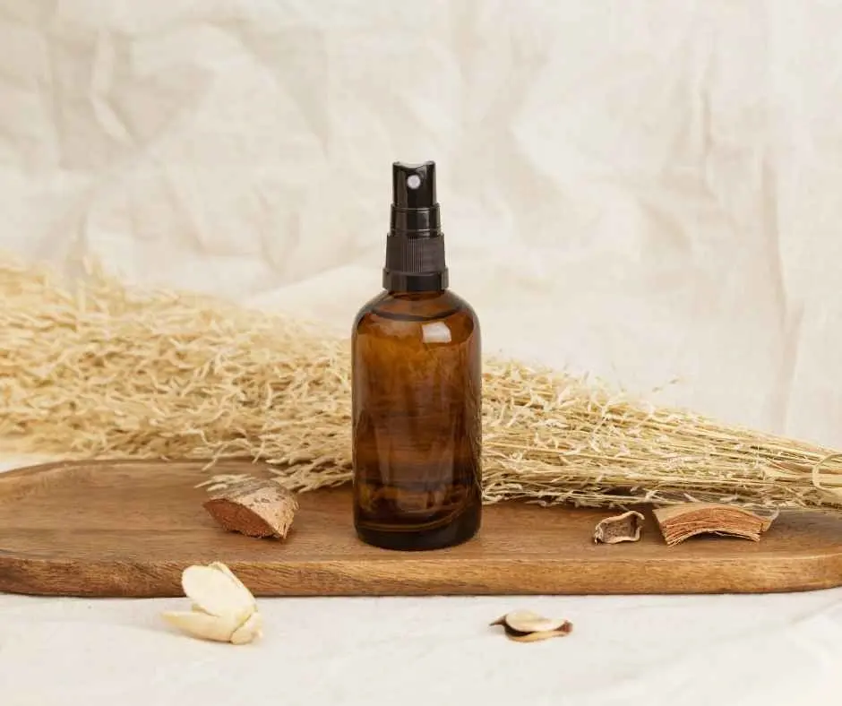 Amber spray bottle with alcohol-based natural fragrance on a wooden tray with dried botanicals.