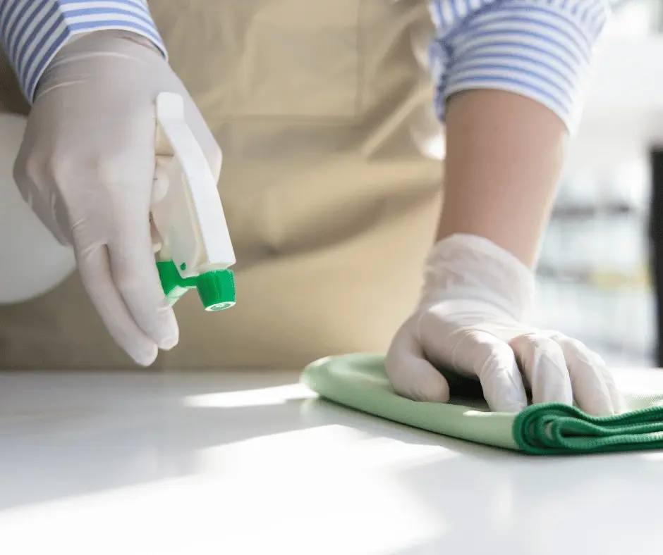 Gloved hand cleaning a surface with a spray bottle of surgical spirit.