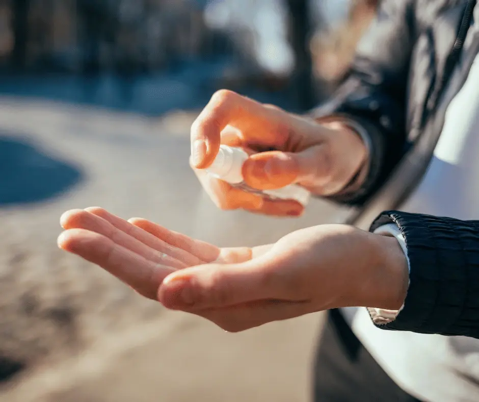 Person applying surgical spirit from a small spray bottle onto hands outdoors.